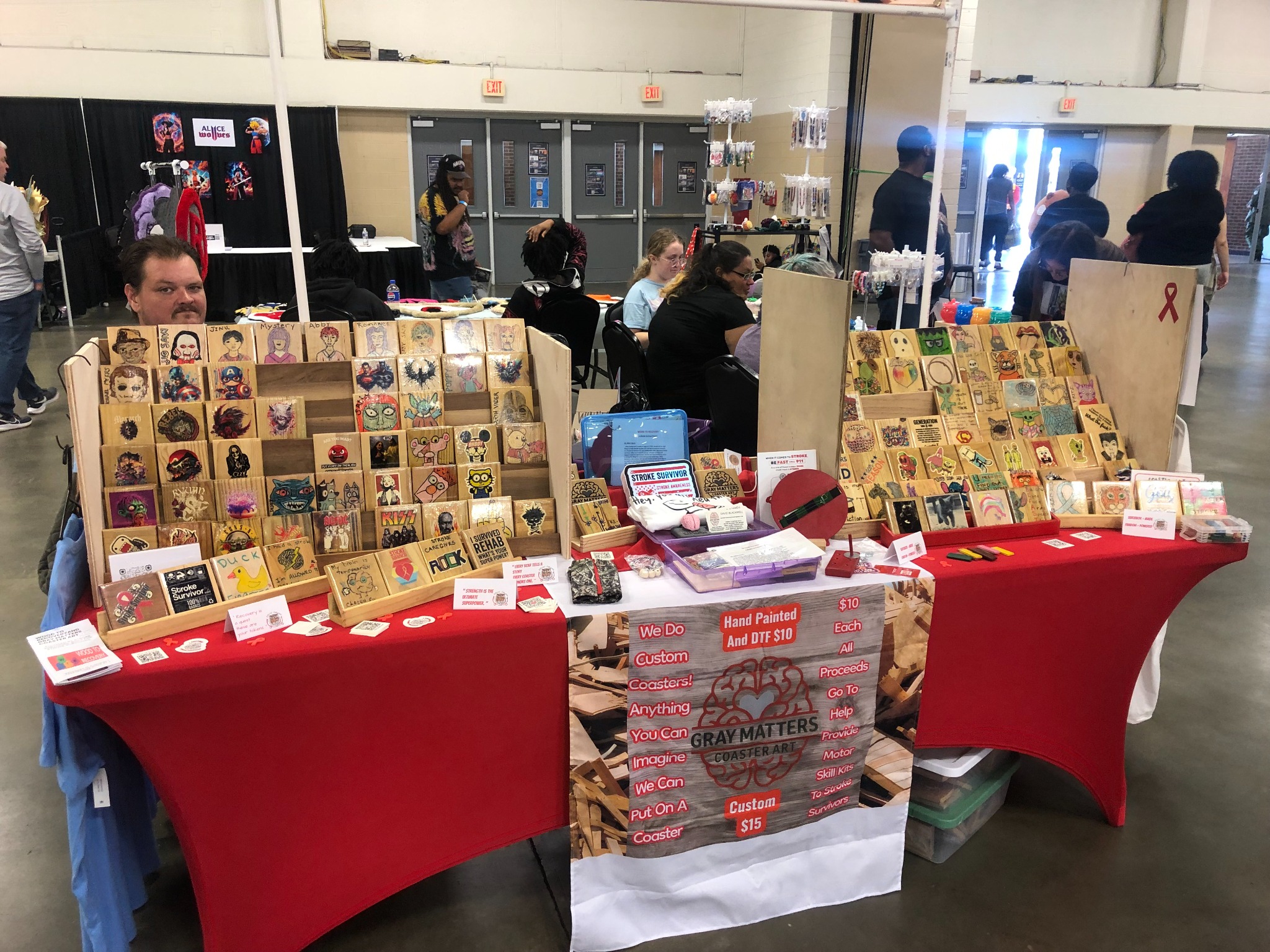 Gray Matters Coaster Art event table with racks of hand-painted wooden coasters and information about recovery kits