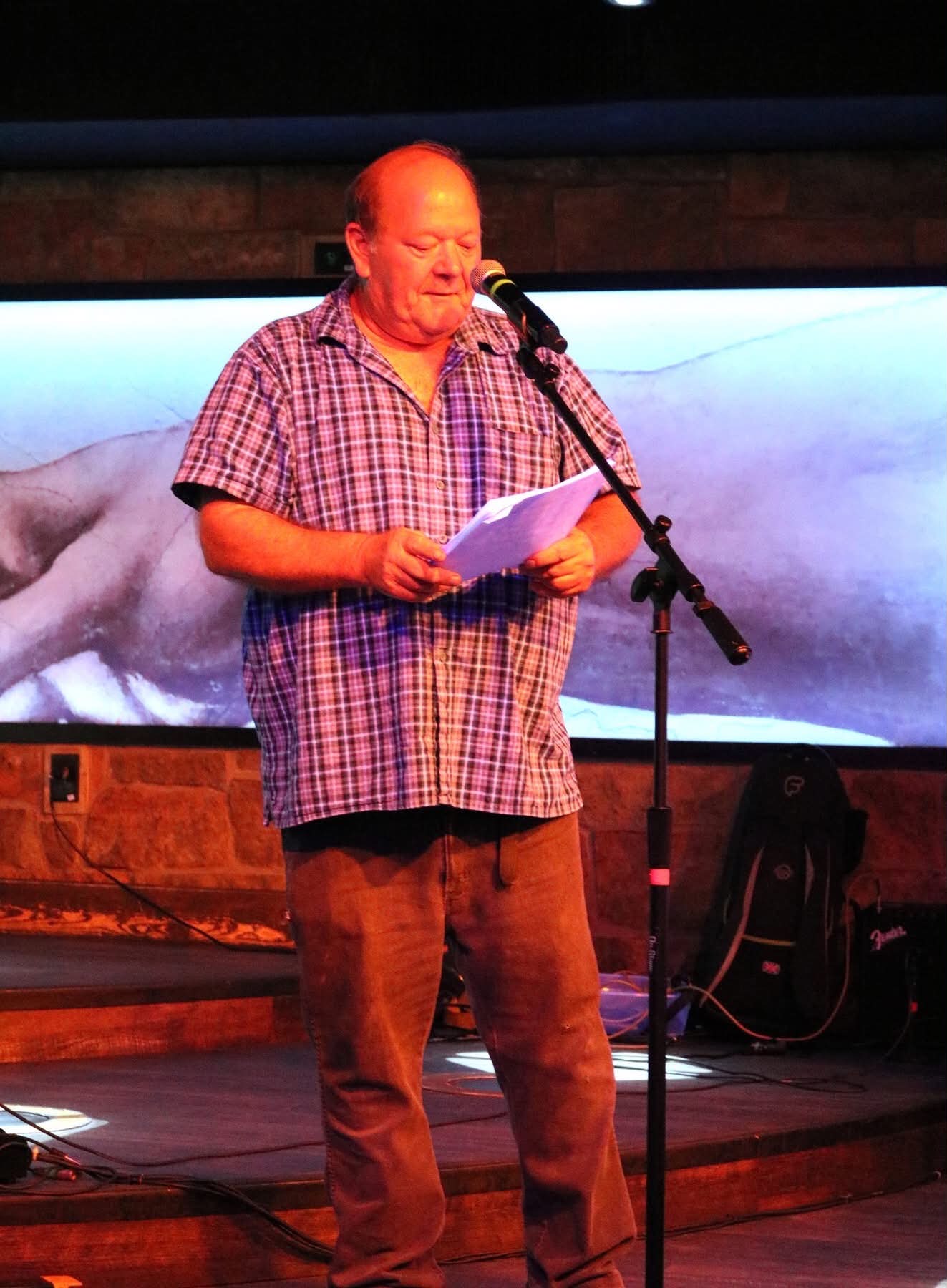 A reader holding papers and speaking into a microphone on stage